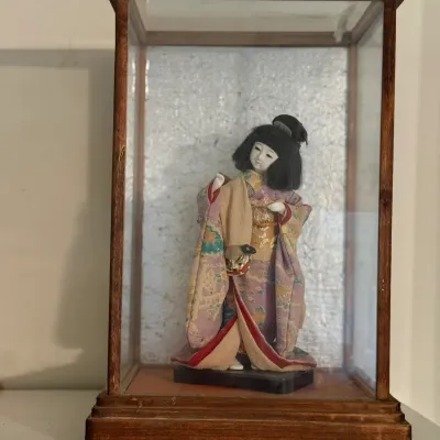 Sale Photo Thumbnail #154: Traditional Japanese geisha doll dressed in an ornate patterned fabric kimono, housed inside a rectangular wooden glass display case.
