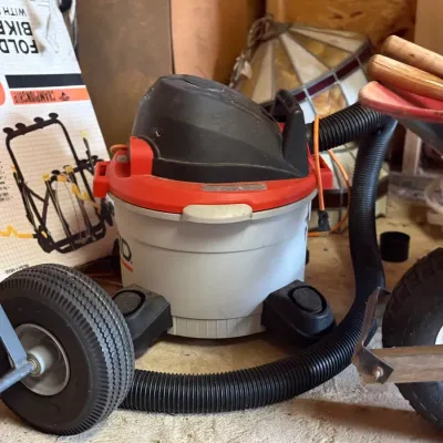 Sale Photo Thumbnail #220: Ridgid portable wet/dry shop vacuum with attached hose, shown stored in a garage alongside hand tools and equipment.