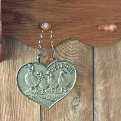 Sale Photo Thumbnail #173: Vintage heart-shaped brass welcome sign featuring relief-embossed ducks with bows, hanging from a small chain.