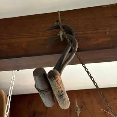 Sale Photo Thumbnail #112: Pair of antique hand-forged iron hay hooks with wooden T-handles hanging from a beam.