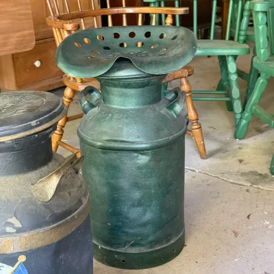 Sale Photo Thumbnail #294: Vintage painted green metal milk can stool repurposed with a tractor seat top, displayed alongside wooden dining chairs and other rustic items.