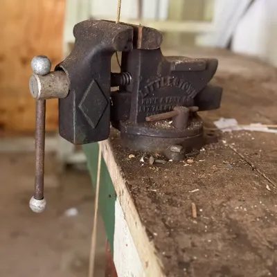 Sale Photo Thumbnail #256: Vintage Littlestown bench vise mounted to a wooden workbench, showing cast iron construction with surface patina and wear.
