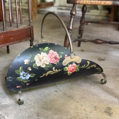 Sale Photo Thumbnail #262: Vintage hand-painted metal log holder with floral motifs and a metal arched handle, resting on scroll feet.