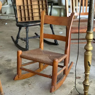 Sale Photo Thumbnail #271: Vintage child's wooden rocking chair with a woven rush seat, displayed alongside other antique furniture pieces.