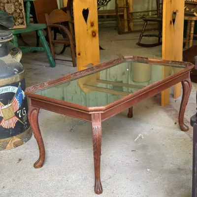 Sale Photo Thumbnail #299: Traditional Queen Anne style wooden coffee table with a mirrored top insert and carved cabriole legs, alongside a light pine quilt rack with heart cutouts.