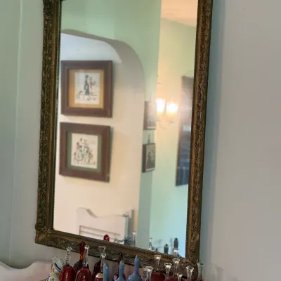Sale Photo Thumbnail #63: Large vintage wall mirror featuring a heavily detailed, ornate antique gold-finished wooden frame, displayed above a collection of colored glass bells.