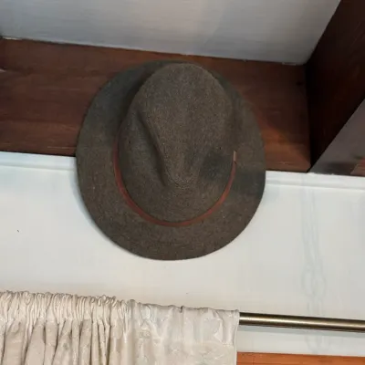Sale Photo Thumbnail #132: Vintage brown wool felt fedora featuring a thin leather hatband, displayed on a wooden surface.
