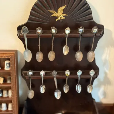 Sale Photo Thumbnail #98: Vintage dark wood wall-hanging spoon rack featuring a carved sunburst design with a brass eagle crest, holding twelve souvenir spoons with enamelled crests.