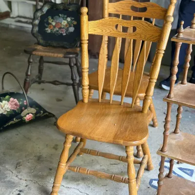 Sale Photo Thumbnail #261: Set of golden oak spindle-back dining chairs with carved top handles, set alongside a small wooden shelf and decor.