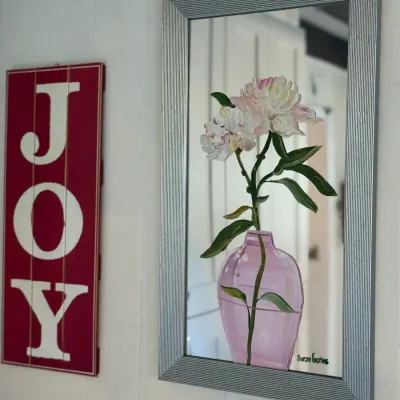 Sale Photo Thumbnail #142: Framed decorative mirror featuring a hand-painted floral design of pink peonies in a purple vase, signed by Susan Goates, alongside a red wooden 'JOY' wall sign.