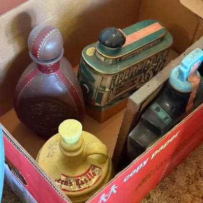 Sale Photo Thumbnail #75: Collection of vintage decorative liquor bottles and novelty ceramic decanters stored inside a cardboard box.
