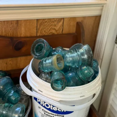 Sale Photo Thumbnail #184: Collection of vintage aqua and clear glass insulator caps stored in a plastic bucket.