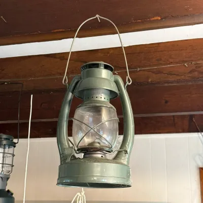 Sale Photo Thumbnail #114: Vintage olive green metal hurricane lantern with a clear glass globe, hanging by its wire bail handle.