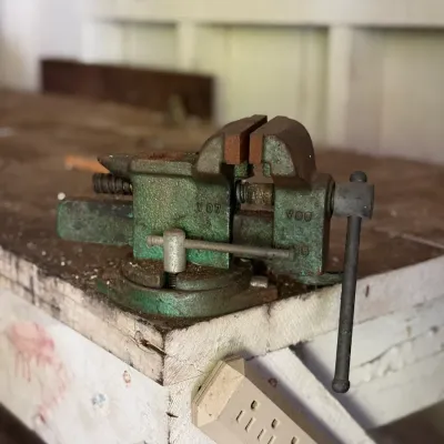 Sale Photo Thumbnail #257: Vintage green cast-iron bench vise mounted on a wooden workbench, showing surface rust and signs of use.