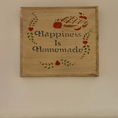 Sale Photo Thumbnail #156: Vintage square wooden kitchen plaque featuring stenciled lettering reading "Happiness Is Homemade" alongside illustrations of an apple pie, hearts, and leafy vines.
