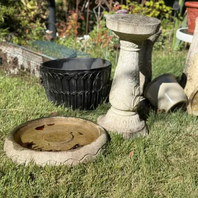 Sale Photo Thumbnail #246: Concrete birdbath stand and dish set alongside a black wrought iron planter and ceramic pots on a grassy lawn.