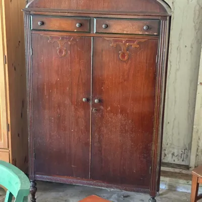 Sale Photo Thumbnail #284: Antique mahogany wardrobe armoire featuring two upper drawers, decorative wood carved accents, a arched pediment top, and turned legs with casters.