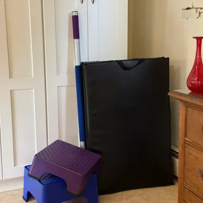 Sale Photo Thumbnail #140: Collection of exercise accessories, including a folded black workout mat, a padded pole, and two plastic step stools in purple and blue.