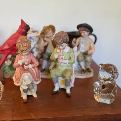 Sale Photo Thumbnail #80: Collection of decorative porcelain and glass figurines, including children figures in vintage attire, a red bird, and a clear glass bear.
