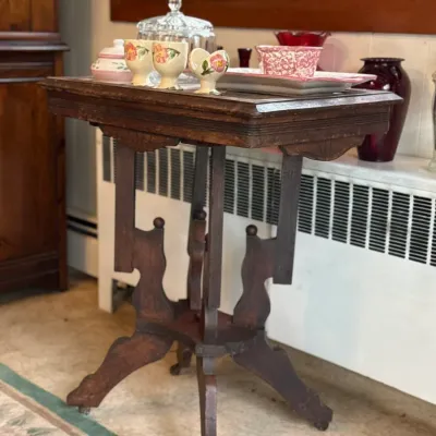 Sale Photo Thumbnail #126: Antique wooden drop-leaf tea cart or accent table featuring ornate carved trestle legs with casters, holding various vintage ceramics and glassware.