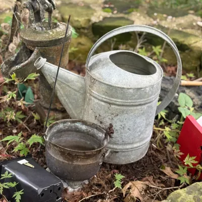 Sale Photo Thumbnail #208: Rustic garden decor assemblage featuring a vintage galvanized metal watering can, a small weathered metal pot, and an antique cast iron hand pump pitcher.