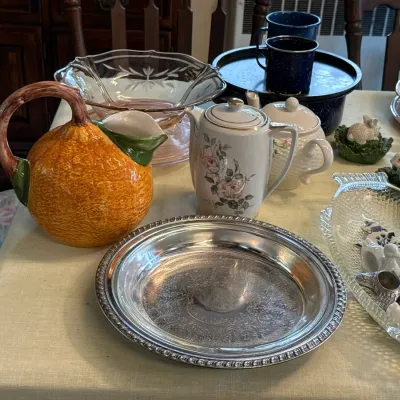 Sale Photo Thumbnail #116: Collection of tabletop items including a vintage ceramic orange-shaped pitcher, a floral porcelain teapot, an etched pink glass bowl, a silver-tone tray, and decorative napkin rings.