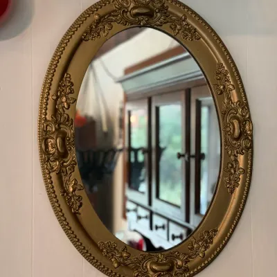 Sale Photo Thumbnail #127: Vintage oval wall mirror featuring a ornate gold-painted frame with beaded trim and floral scrollwork accents.