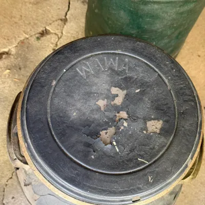 Sale Photo Thumbnail #295: Vintage Wawa metal milk can with flaking black paint on the lid, revealing underlying metal.