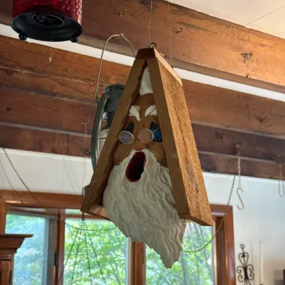 Sale Photo Thumbnail #111: Hand-carved wooden Santa Claus birdhouse designed to hang from the ceiling, featuring small wire-rimmed glasses and a textured white beard.