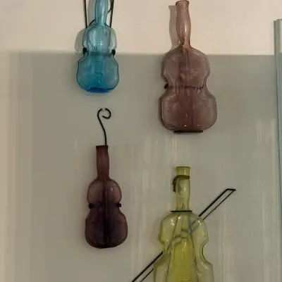 Sale Photo Thumbnail #155: Collection of four vintage violin-shaped colored glass bottles with metal wall mounts, displayed in various shades of blue, purple, and green.