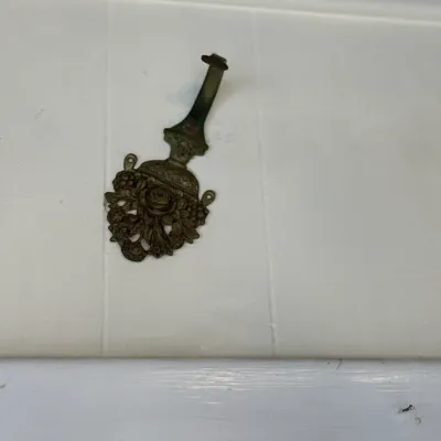 Sale Photo Thumbnail #102: Ornate brass wall hook with intricate floral motifs and a vintage aged patina.