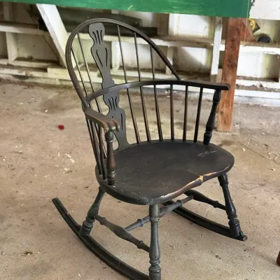 Sale Photo Thumbnail #275: Vintage dark-painted wooden Windsor-style rocking chair featuring turned legs, armrests, and a decorative carved central back slat.