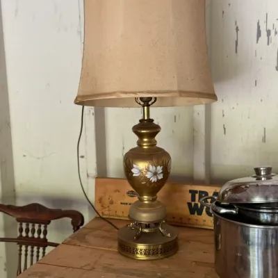Sale Photo Thumbnail #278: Vintage brass-finish table lamp with hand-painted floral details on an urn-shaped body, topped with a tall beige lampshade.