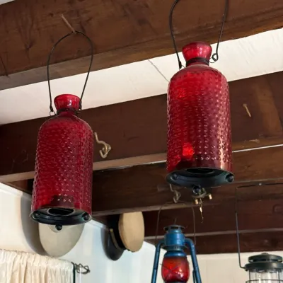 Sale Photo Thumbnail #115: Pair of hanging red hobnail glass candle lanterns, shown suspended from wooden ceiling beams alongside vintage kerosene lamps.