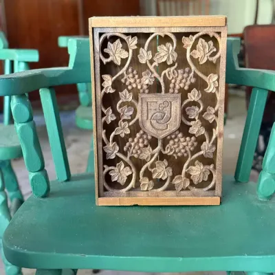 Sale Photo Thumbnail #273: Hand-carved wooden box featuring an ornate grapevine and crest design, displayed on a green painted wooden chair.