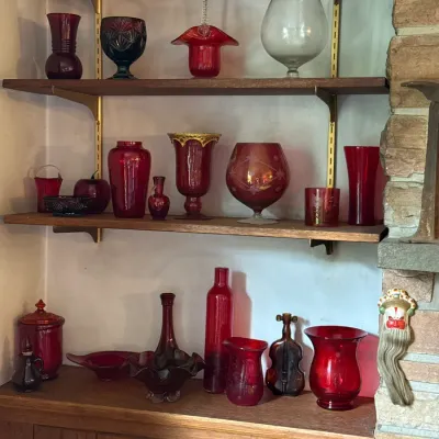Sale Photo Thumbnail #97: Collection of vintage red and ruby glassware, including vases, goblets, and decorative bottles, displayed on mid-century modern wooden shelving.