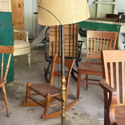 Sale Photo Thumbnail #269: Vintage floor lamp featuring a distressed gold and textured dark pole, decorative ornate base, and a whipstitched parchment drum shade, surrounded by various antique wooden chairs.