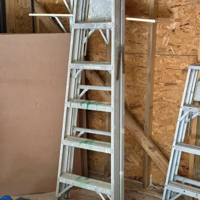 Sale Photo Thumbnail #227: Tall aluminum step ladder showing light wear and green paint marks, stored in a shed.