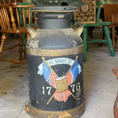 Sale Photo Thumbnail #297: Vintage painted metal milk can featuring Bicentennial patriotic artwork reading "The Spirit of 1776" with crossed flags and a drum. Shows authentic wear, paint chipping, and distressing throughout.