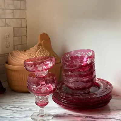 Sale Photo Thumbnail #118: Cranberry cut-to-clear glass tableware set featuring wheel-etched floral motifs, including plates, small bowls, and stemware.