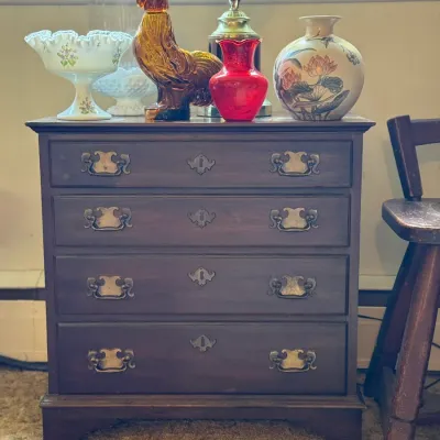 Sale Photo Thumbnail #84: Traditional dark wood four-drawer chest topped with decorative glassware and ceramics, including a amber glass rooster figure, a ruby red vase, and a painted lotus ginger jar.