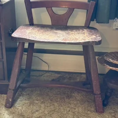 Sale Photo Thumbnail #95: Vintage dark stained wooden low chair or bench featuring a wide contoured seat and decorative back splat, displaying significant finish wear and distressing.