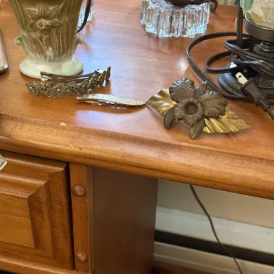 Sale Photo Thumbnail #36: Collection of vintage hair accessories including a floral motif clip and rhinestone barrettes, resting on a wooden desk alongside small lamps and pottery.