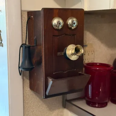 Sale Photo Thumbnail #148: Vintage-style wooden wall-mounted crank telephone novelty reproduction, featuring brass ringer bells and a black ear trumpet receiver.