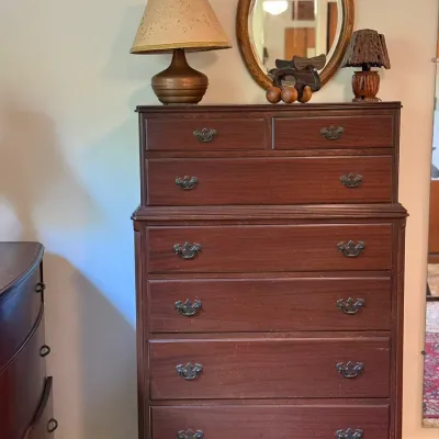 Sale Photo Thumbnail #45: Traditional dark mahogany tall chest of drawers with batwing brass pulls and bracket feet, topped with a small oval wall mirror, table lamps, and decorative accessories.