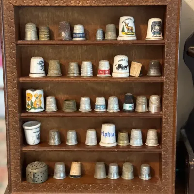 Sale Photo Thumbnail #99: Vintage collection of metal and porcelain thimbles, displayed in a wooden shadow box with carved border detail.