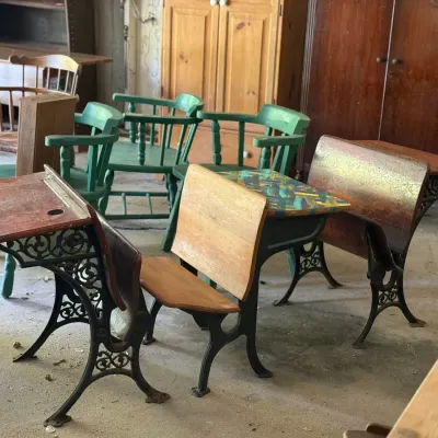 Sale Photo Thumbnail #288: Collection of antique cast iron and wood school desks alongside painted green wooden captains chairs and various furniture pieces.