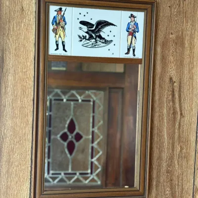 Sale Photo Thumbnail #194: Vintage wood-framed wall mirror featuring decorative Bicentennial-style printed tiles depicting Revolutionary War soldiers and an American eagle.