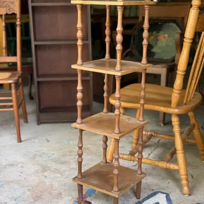 Sale Photo Thumbnail #260: Vintage four-tier wooden shelf with turned spindle supports and top finials, surrounded by wooden chairs and a bookcase.