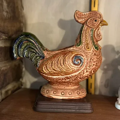 Sale Photo Thumbnail #90: Vintage stylized ceramic rooster figurine mounted on a wooden base, featuring detailed textured carving and colorful glazed accents.